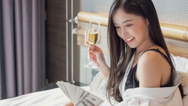 ベッドでシャンパンとお札を持つ女性