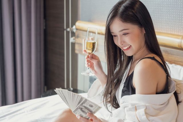 ベッドでシャンパンとお札を持つ女性